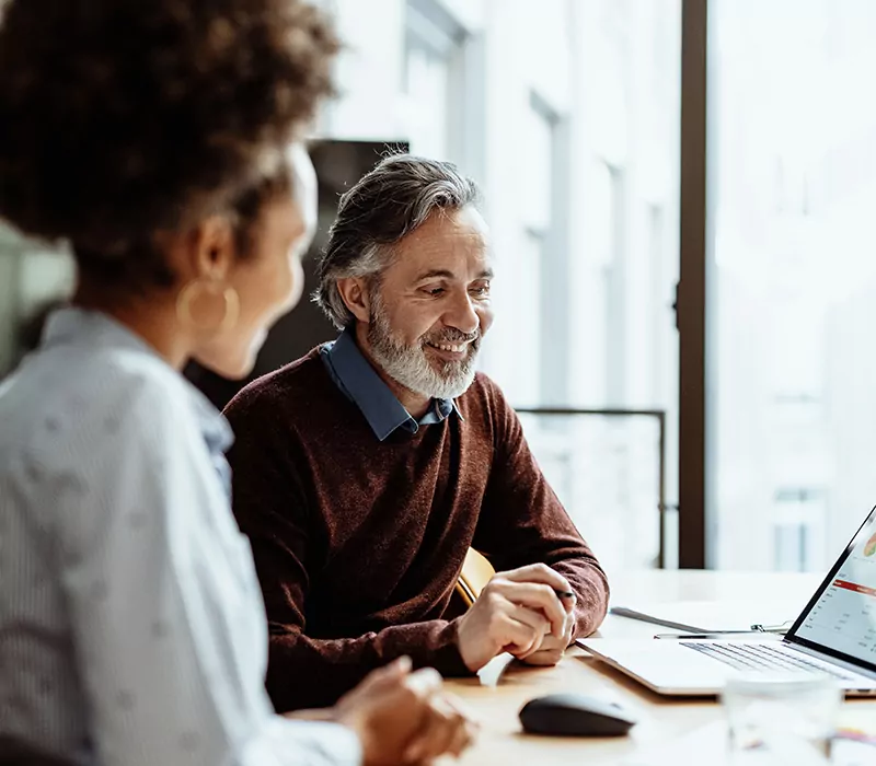 smiling financial advisor and business person talking to mixed race female colleague in office